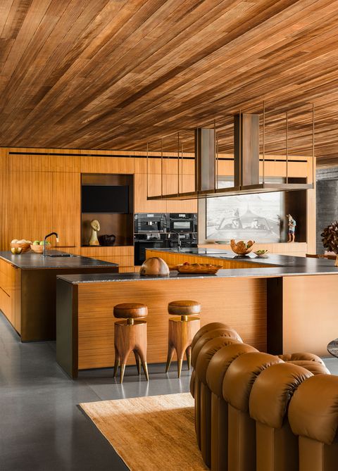 teak open plan kitchen with long l shaped counters with black tops and designy wooden stools