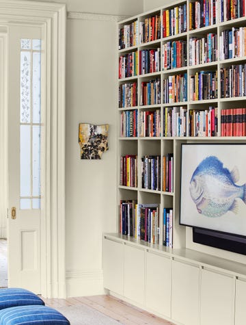 a living room has built in shelves and cabinets along a wall that also houses a frame television by samsung that has a picture of a colorful fish, sliding doors with decorate glass and two navy stools with white stripes