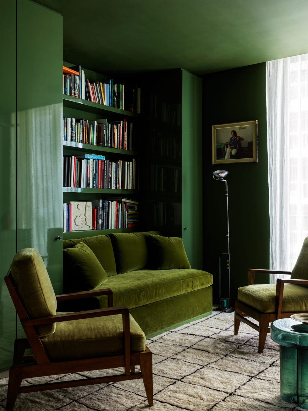 a study is done in shades of green the sofa and chair cushions are in a moss, lacquered cabinets are in a traditional green, a round side table is an emerald green, shelves behind sofa, light rug with black lines