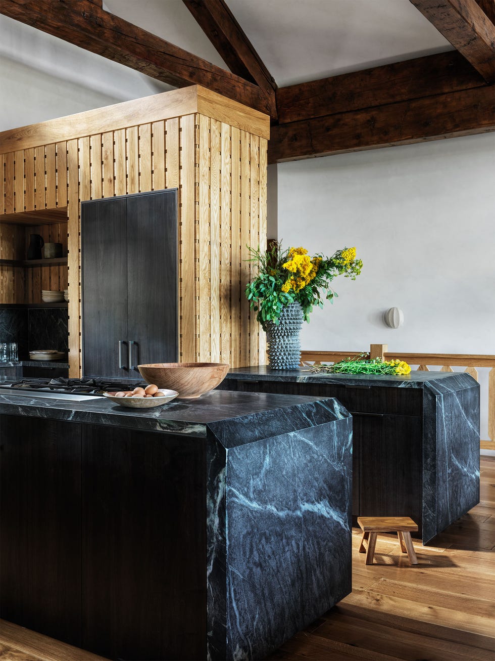two dark marble islands with light veining and a back slatted wall wth built in shelves and cabinetry and a plant wood floor in natural