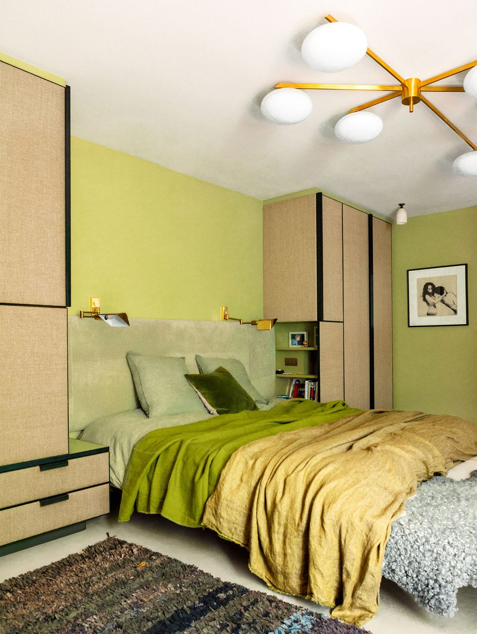 Retrouvius - ELLE DECOR bedroom with tall light green headboard and flanked by floor to ceiling simple cabients on either side and a green and yellow duvets