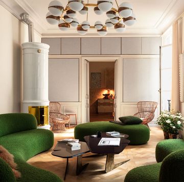 expansive european looking living space with multiple curvy seating sofas in a lush dark green and an extravagant but simple chandelier of multiple white builbs with gold bands and a double tier cocktail table