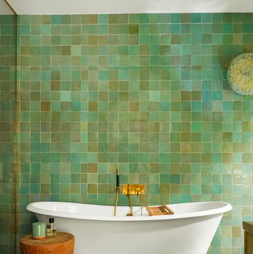 bathroom with white claw foot tub and stump like wooden table and a wall of tiles in multiple shades of green