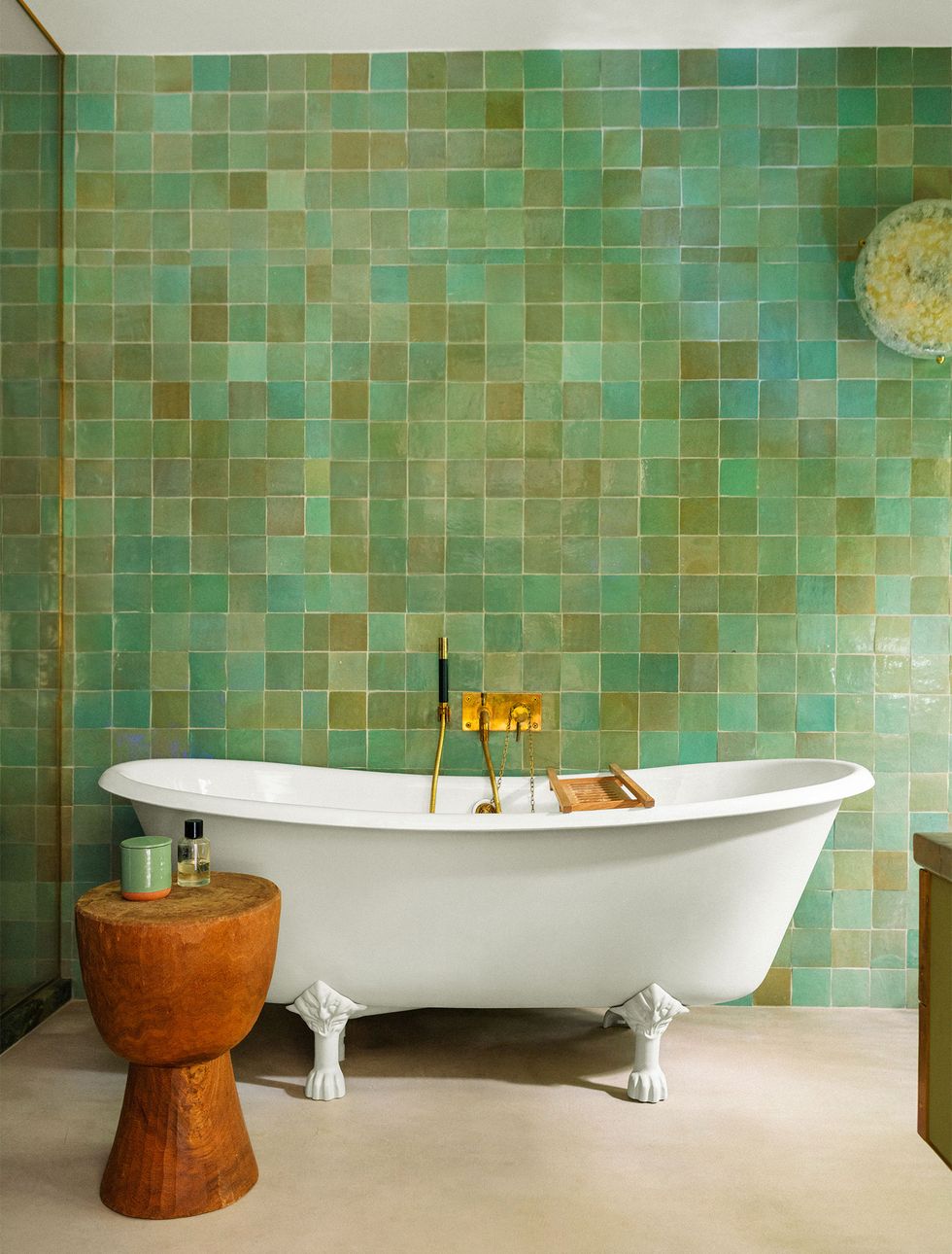 bathroom with white claw foot tub and stump like wooden table and a wall of tiles in multiple shades of green