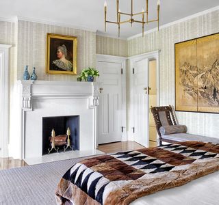 bedroom with fireplace, white walls, painting, and bed with brown and black patterned throw