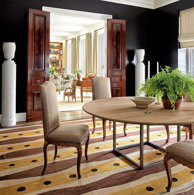 dining room with large pedestal table and queen anne type upholstered chairs all in light colors on a matisse inspired patterned rug and the room is connected to the living room by two tall wood doors with brass handles
