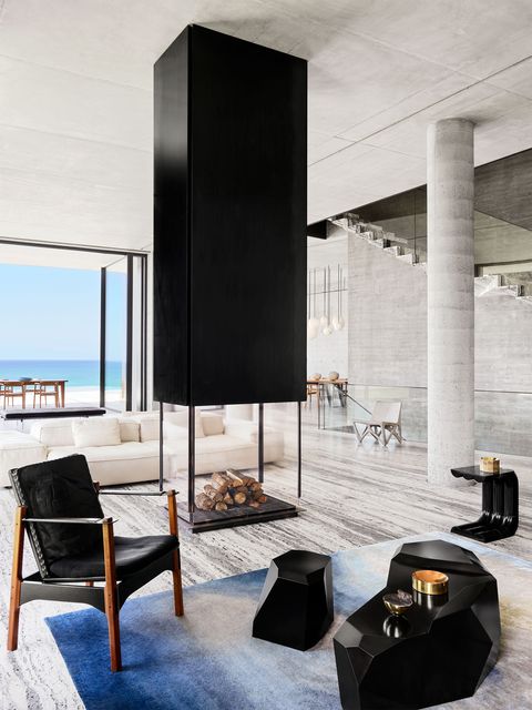 open living area with doors to the mediterranean and black accent furniture and rock shaped tables on a moire blue area rug and a tall monolithic fireplace at center a