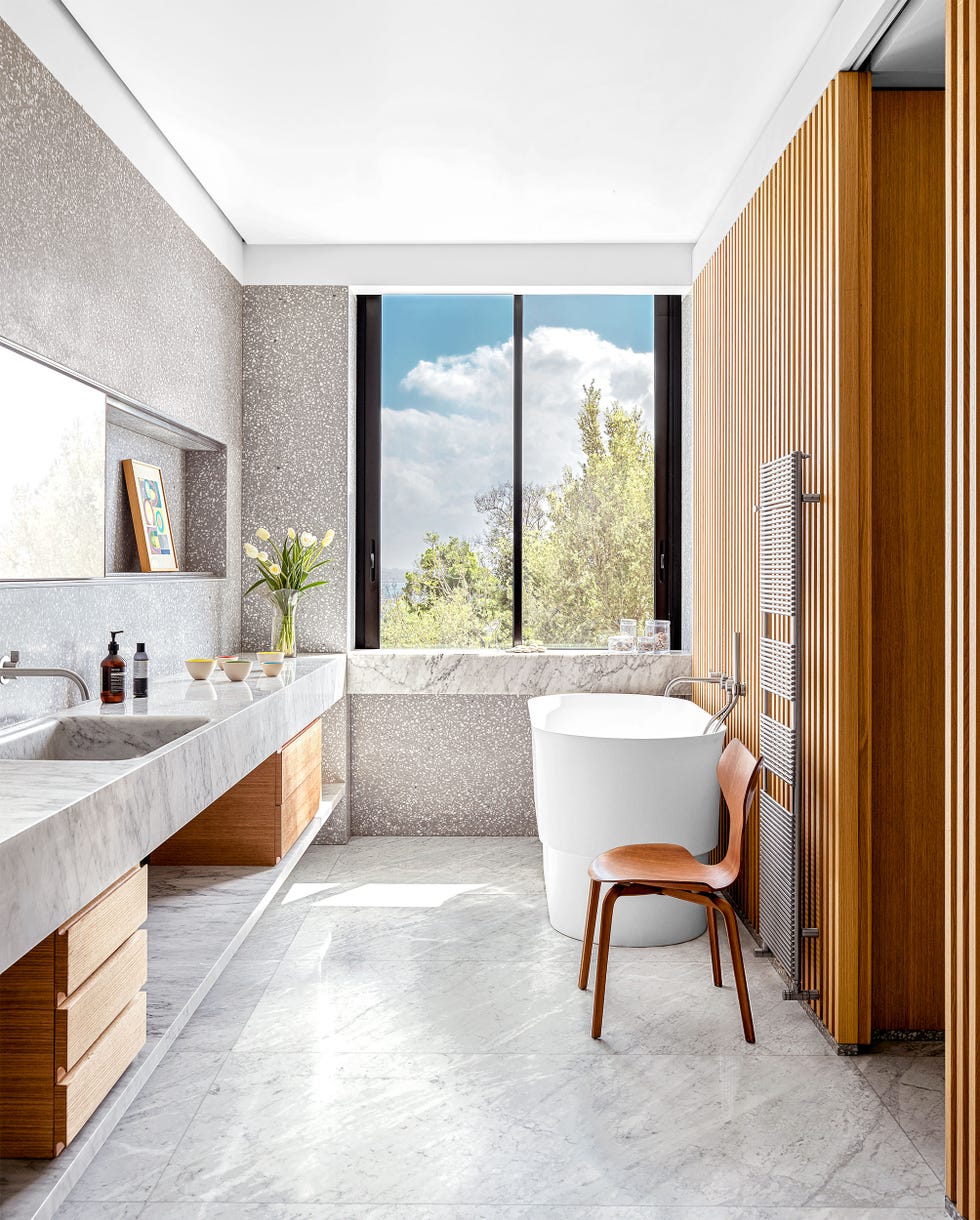 Raëd Abillama - ELLE DECOR bathroom with marble slap counter and inset since and matching floor with light cabinets for storage underneath and an oval standalone tube again the slatted walls also in light wood