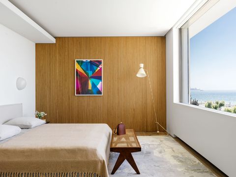 spare bedroom with ribbed paneling in a honey oak color with some art on it and a camel colored bedspread with fringe and the bed is facing a long window with even more view of mediterranean that you can imagine waking up to