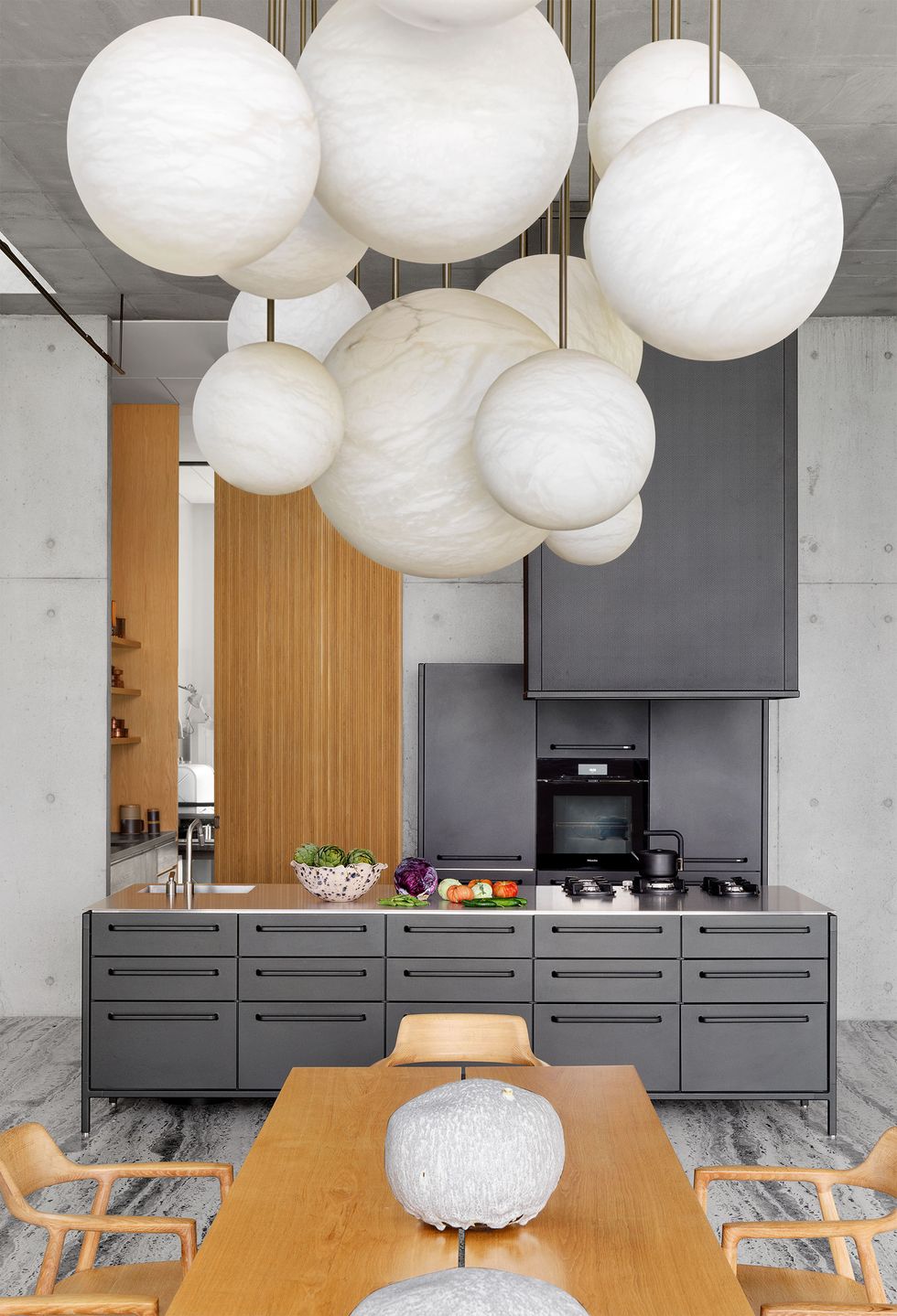 sleek gray kitchen at the end of a light wood dining table and chairs with a globular pendent chandelier above