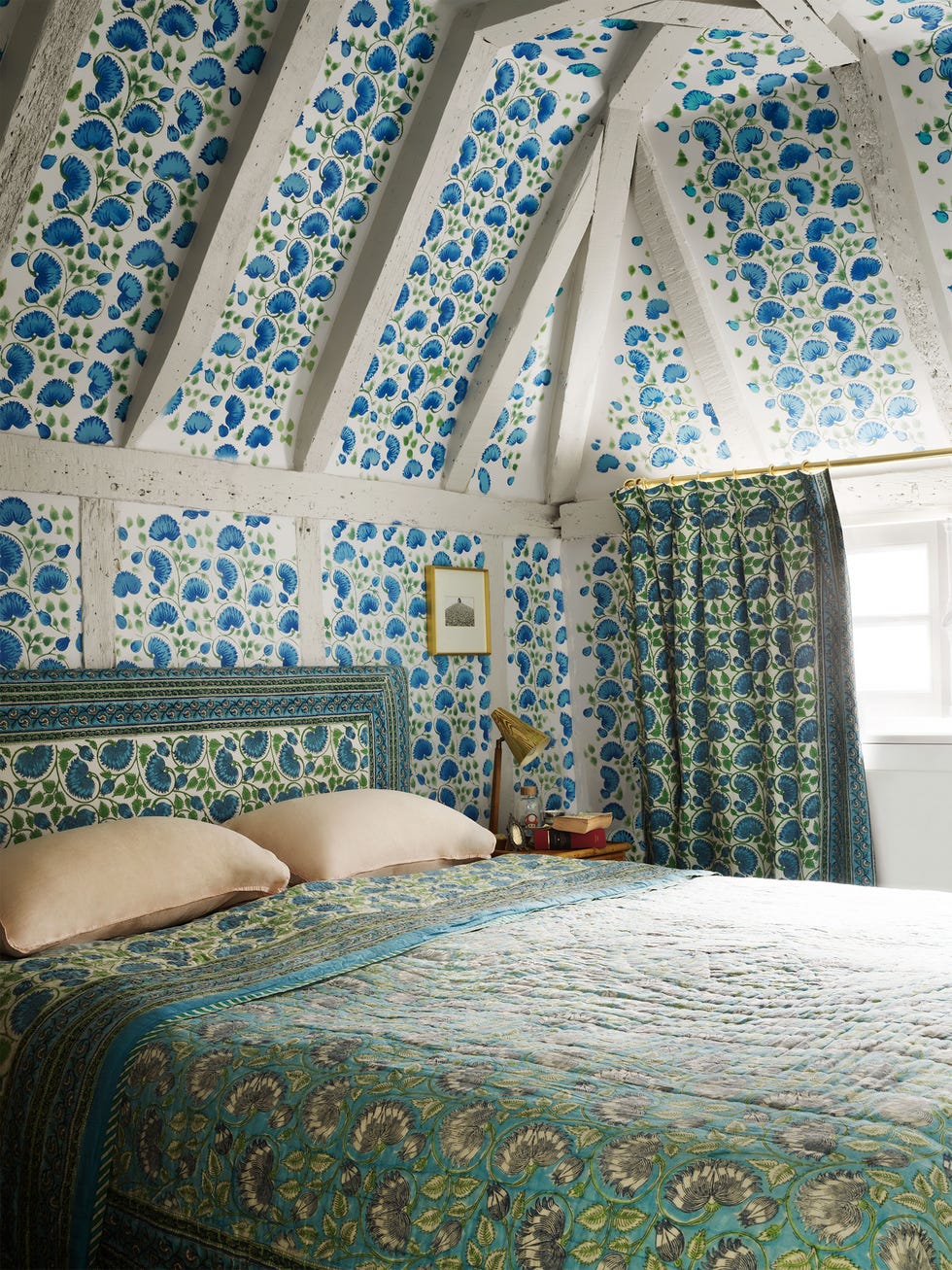 chambre avec avant-toit et plafond à poutres et murs et plafonds à motifs bleus avec un couvre-lit vert complémentaire avec des formes similaires en gris dessus et une tête de lit rembourrée