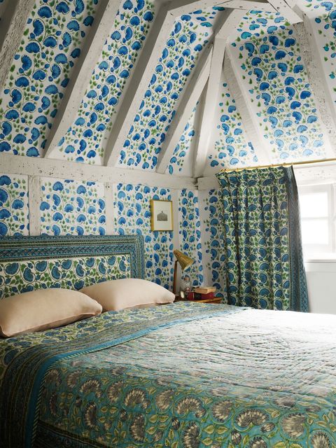 bedroom with eaves and beamed ceiling and a blue pattern stamped walls and ceilings with a complementary green coverlet with similar shapes in gray on it and an upholstered headboard