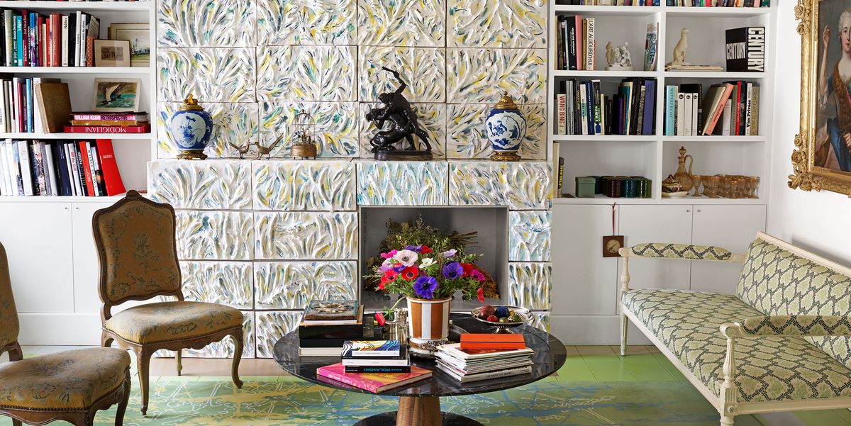 living room area with large tiled wall with inset for a planter and built in bookshelves on either side and some chairs and a settee in a chain link pattern upholstery and a round low pedestal table at center heaped with books on a green rung