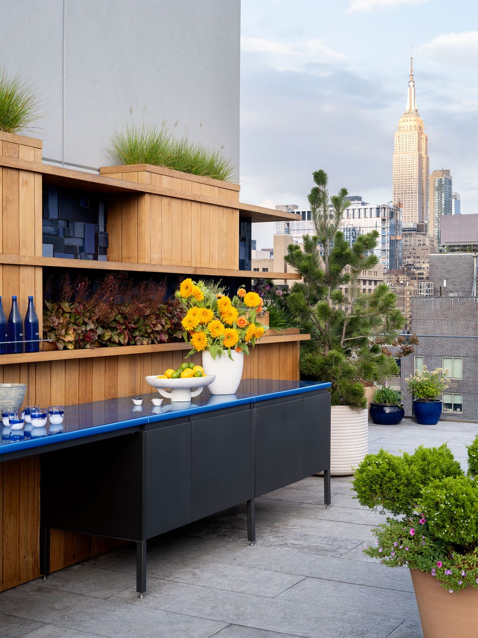 rooftop terrace - ELLE DECOR outdoor kitchen counter in blue with yellow flowers in a white vase atop it and the manhattan skyline in the background
