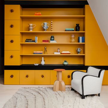yellow built in shelves with black trim and a neutral shaggy design carpet and white club chair with black trim and a small low wood table with a small orange top