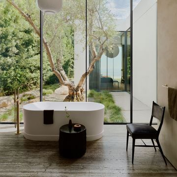 a chair and a lamp in a bathroom with a large window and a oval standalone tub