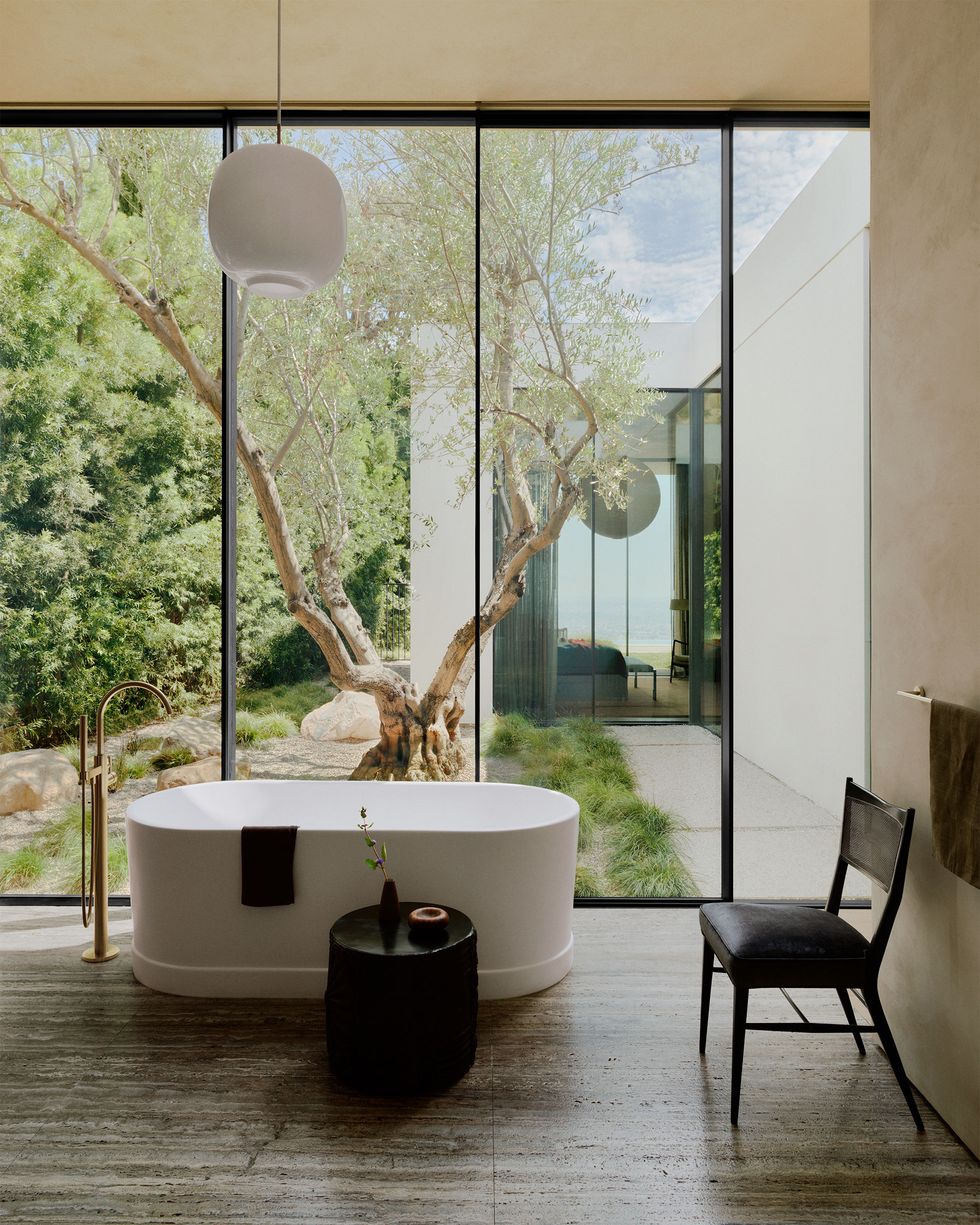 a chair and a lamp in a bathroom with a large window and a oval standalone tub