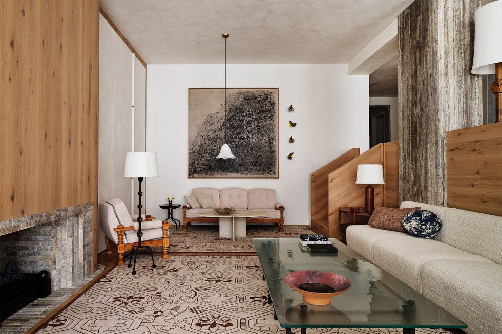 sunken living room with a boucle sofa against a half wall, glass topped cocktail table, seating area with loveseat with pendant and chair with floor lamp, low set stone fireplace with wood paneling above