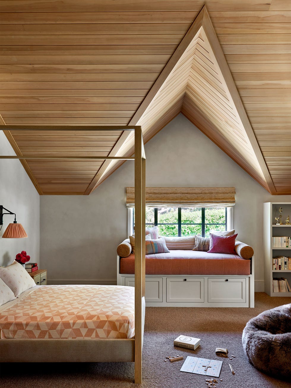 child's bedroom light walls, pitched wood beadboard ceiling, window with cushioned seat and storage beneath, wood canopy bed, geometric patterned bedcover, bookcase, furry beanbag chair, carpet