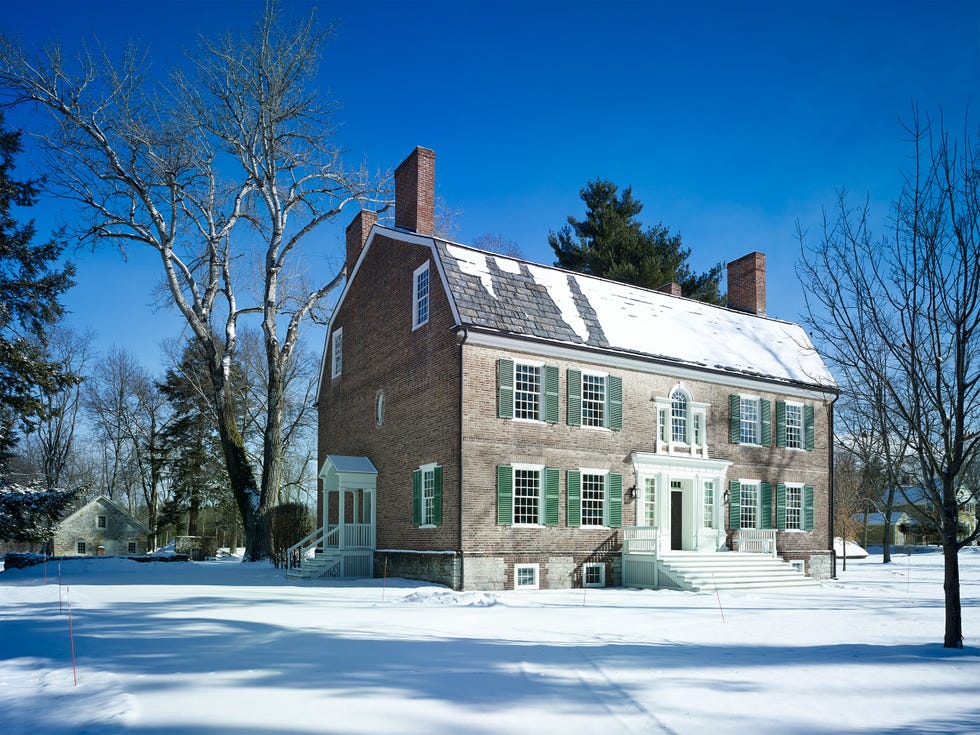 classic georgian style house with multiple window on the face with green shtters and majestic white stairs leading up to the front door all set in a snowy landscape