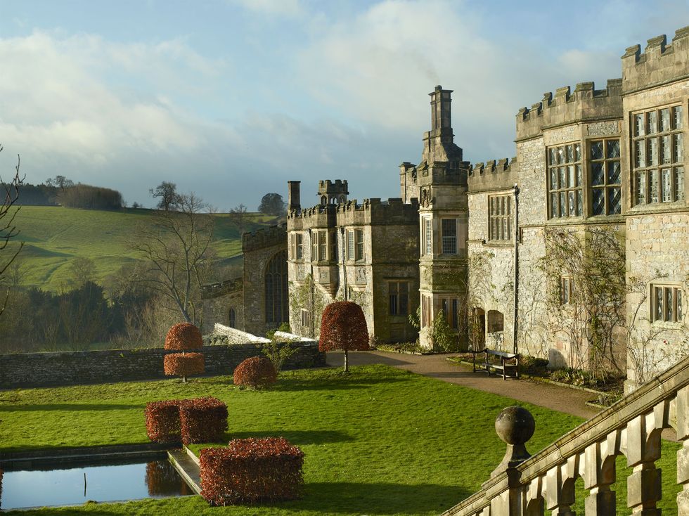 A large English mansion building made of stone and in front of it is a spacious garden