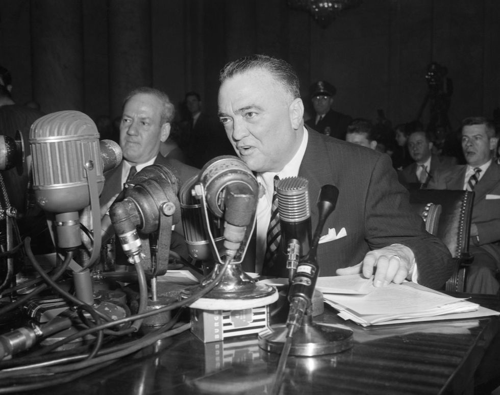 j edgar hoover sitting at a desk in front of microphones and speaking