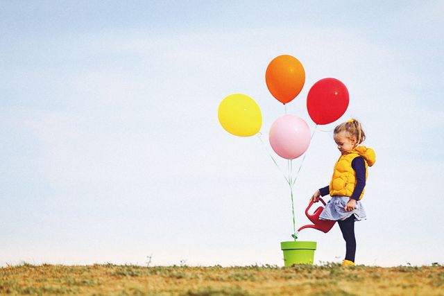 Cute blonde little girl is seeding and watering colorful balloons