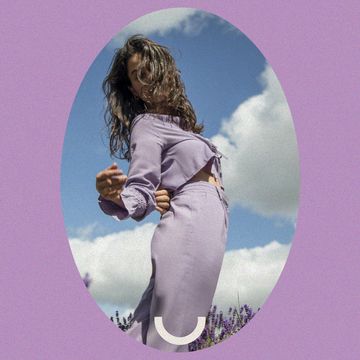 a woman standing in a purple garment in front of clouds