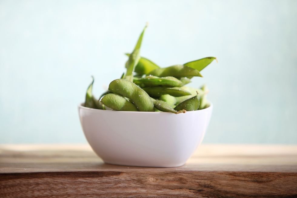 a bowl of edam soy beans in the pod, sitting on a wood board