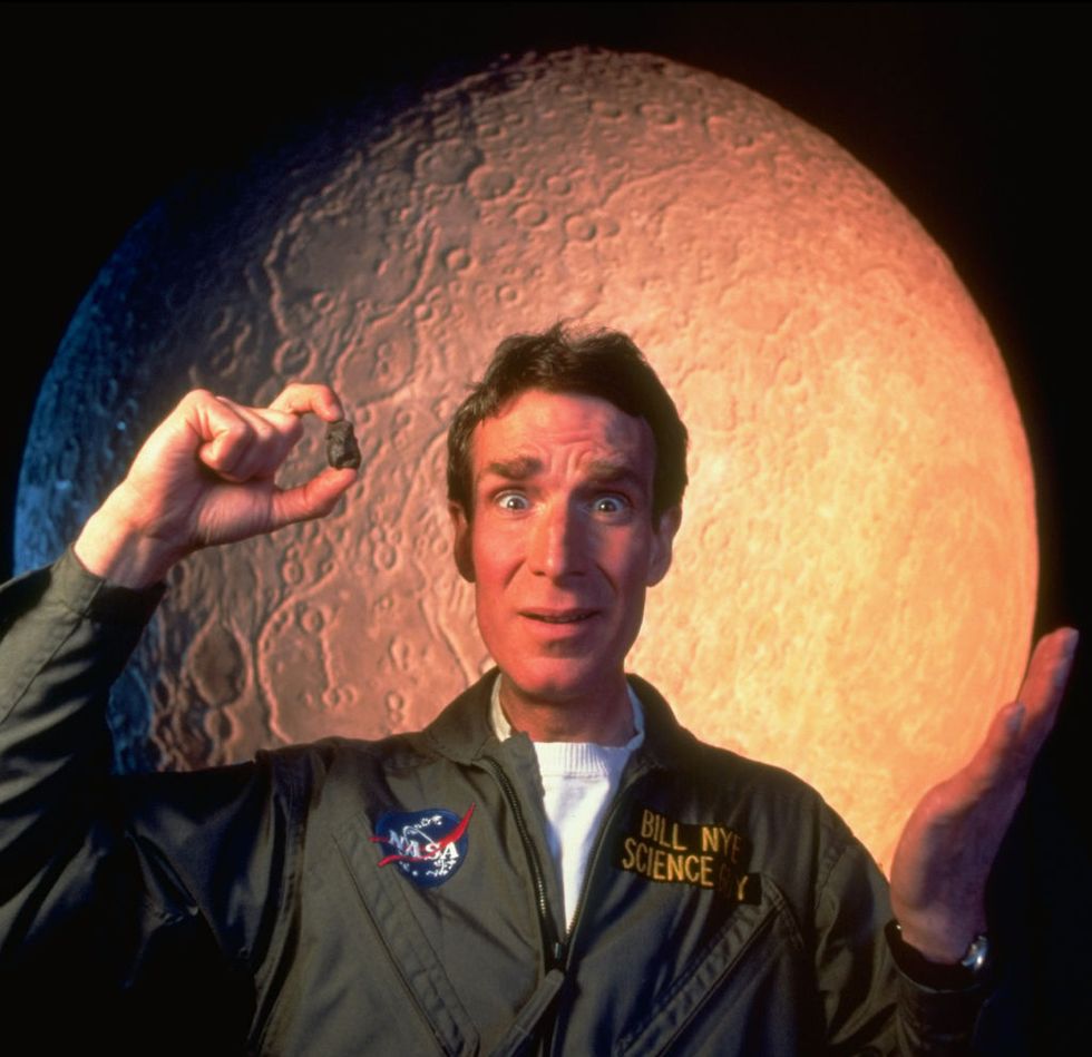 Scientist Bill Nye in a space suit standing in from of the moon
