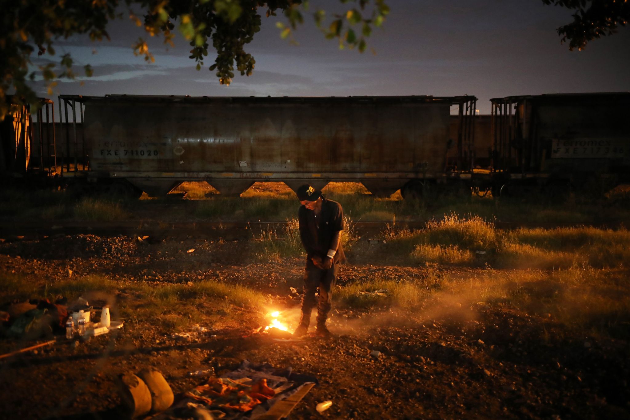 a man stands next to a trash fire in the waste ground next to the malverde shrine