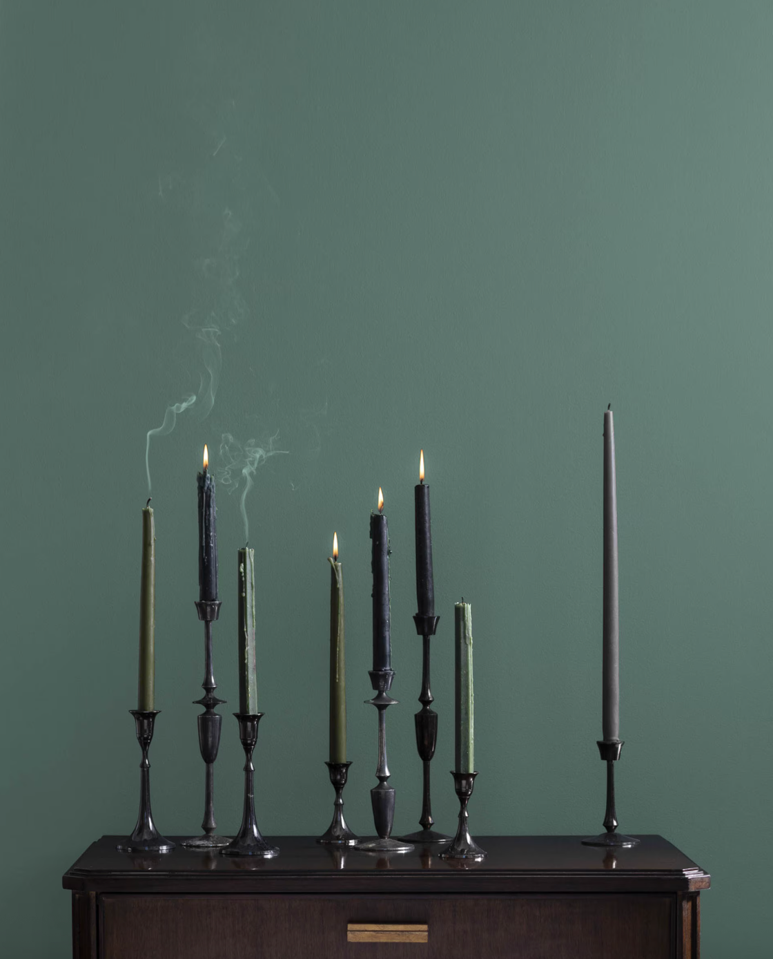 Candles lit and extinguished on a dark wooden surface against a green wall.