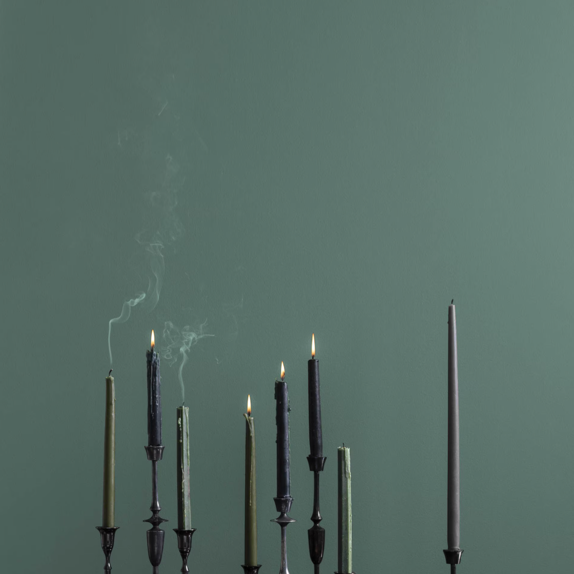 Candles lit and extinguished on a dark wooden surface against a green wall. Candles lit and extinguished on a dark wooden surface against a green wall.