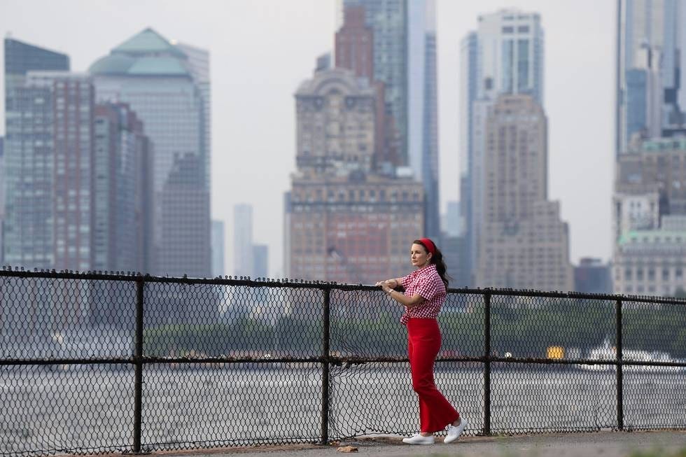 A person stands by a railing overlooking a river and skyline.