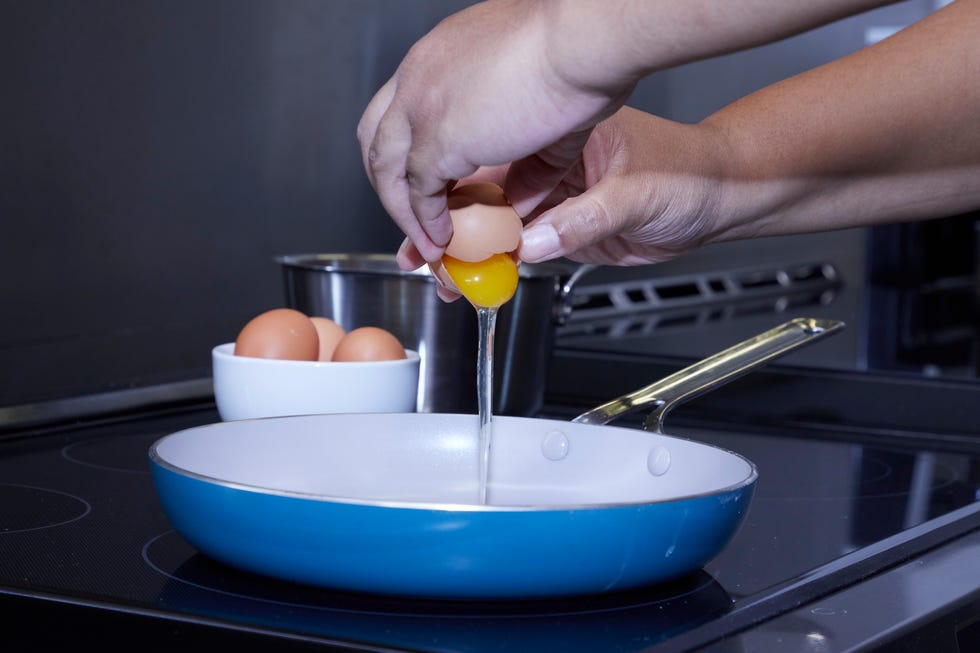 a person cracking an egg over a pan on an induction cooktop stove