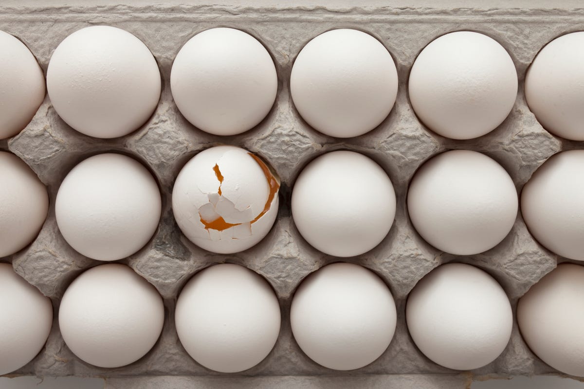 A carton containing white eggs with one cracked egg revealing yellow yolk