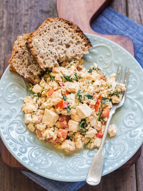 vegan tofu scramble with tomato and green herbs served with wholegrain homemade bread wooden background