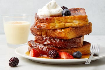 eggnog french toast topped with whipped cream and berries on a plate with a glass and jug of eggnog in the background