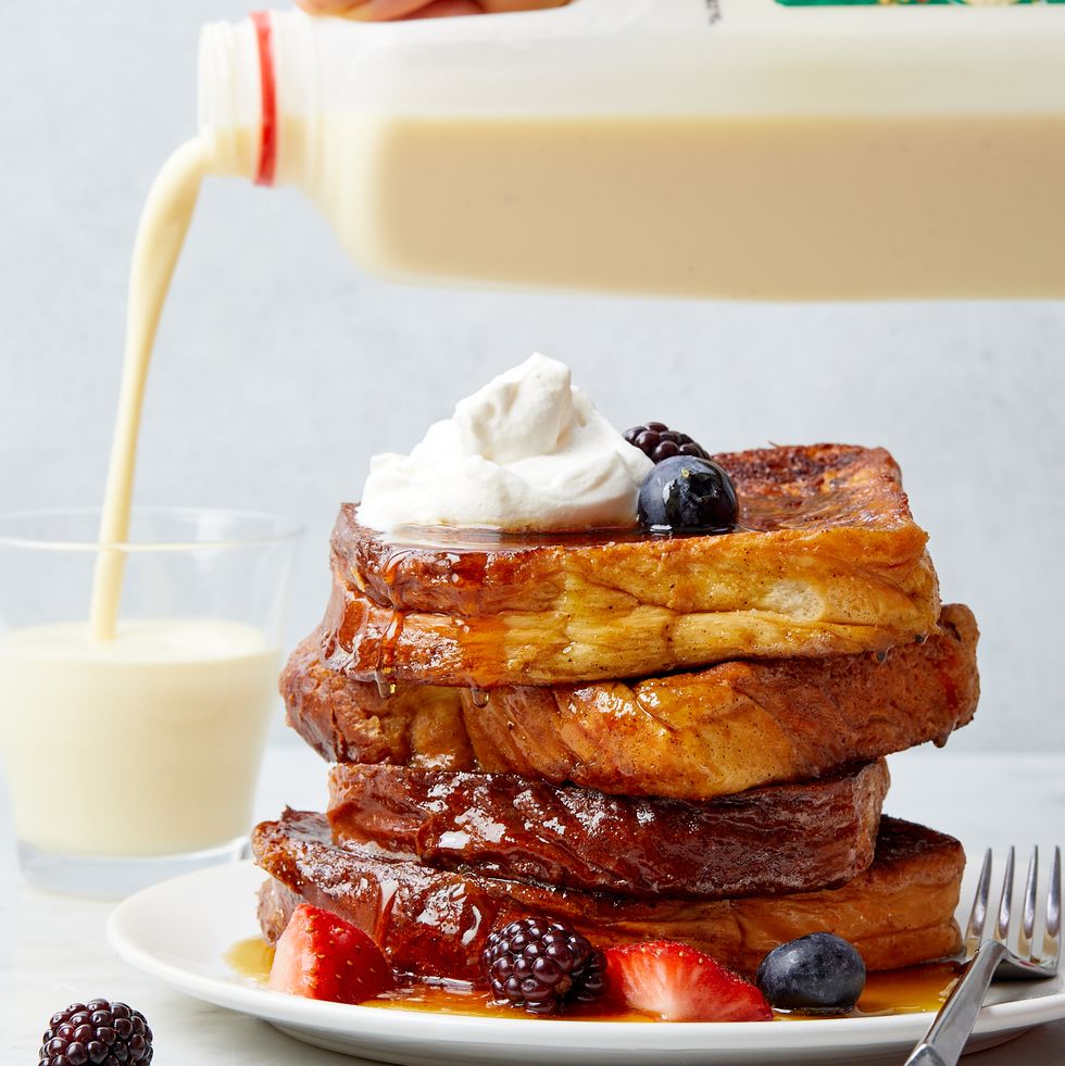 eggnog french toast topped with whipped cream and berries on a plate with a glass and jug of eggnog in the background