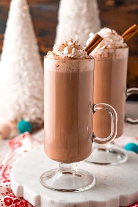 eggnog hot chocolate in glass mug with whipped cream and cinnamon stick
