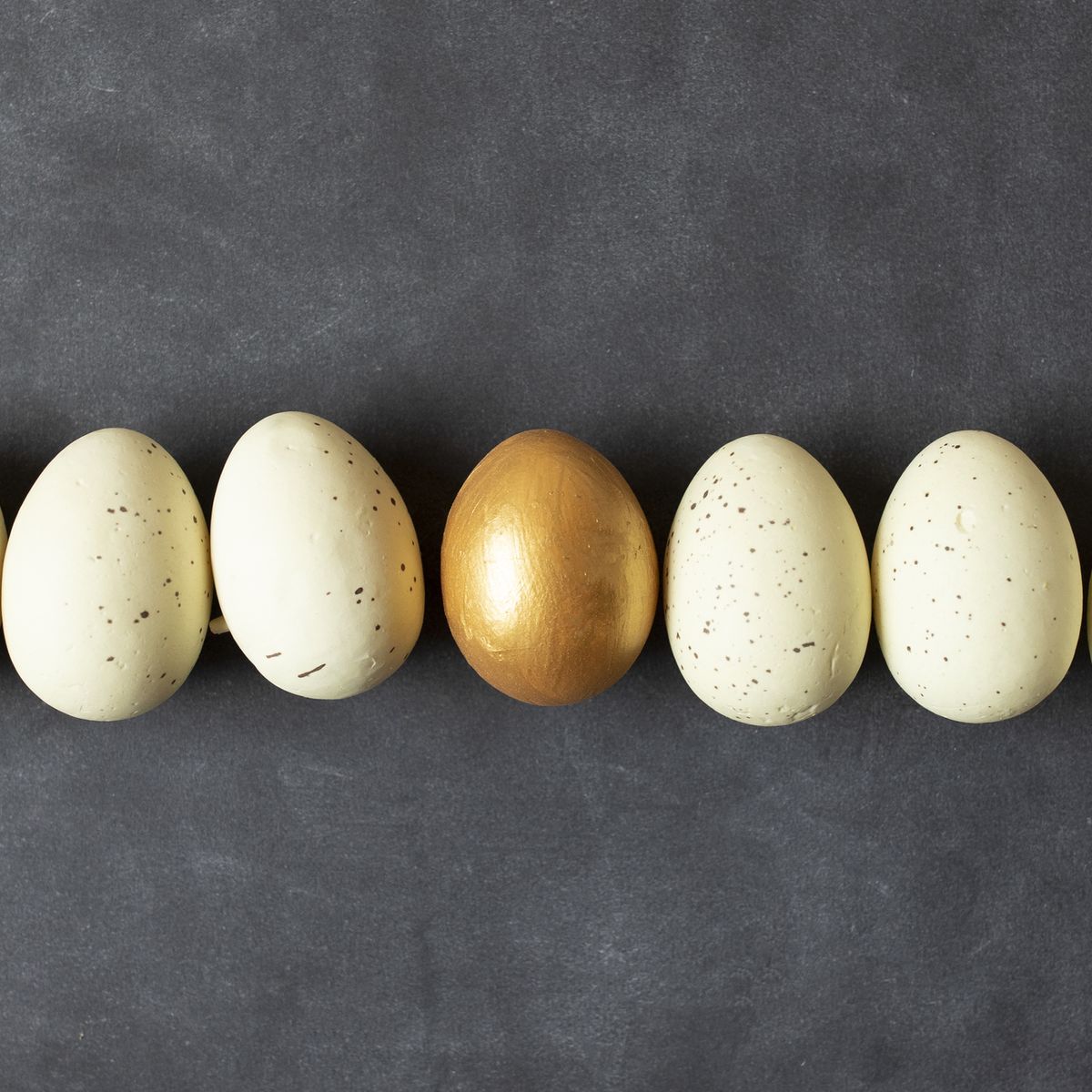 Eggs and one golden egg in nest basket on the black background.