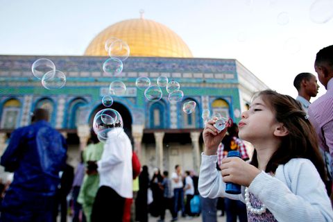 Een meisje blaast bellen voor de gouden koepel van de AlAksamoskee op de eerste dag van het Suikerfeest in de Oude Stad in Jeruzalem