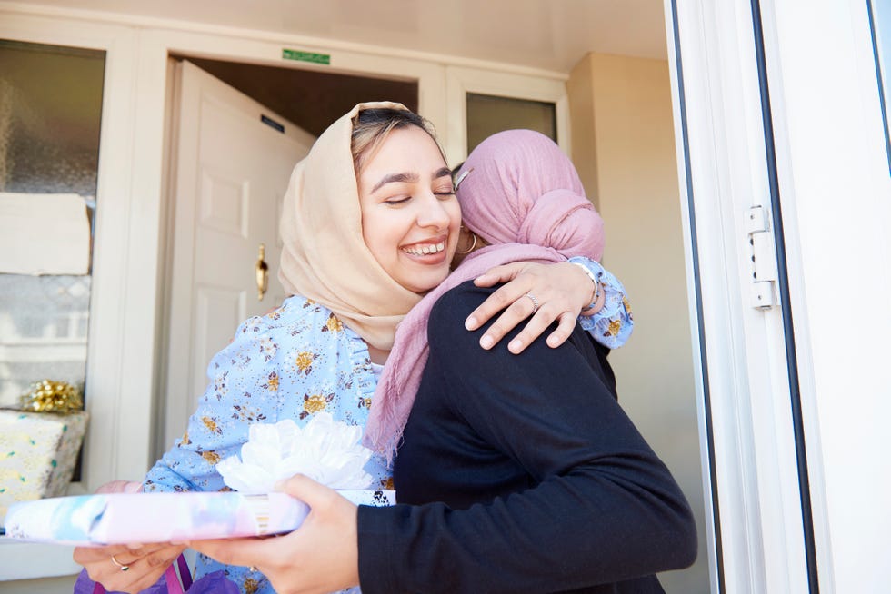 young woman welcomes and hugs a friend holding a gift to eid al fitr celebration