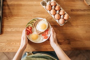 een vrouw houdt een bord met ei, tomaat en avocado vast