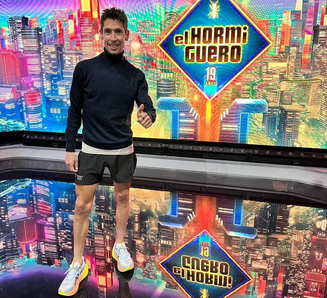 person giving a thumbsup in a studio setting with a colorful cityscape background