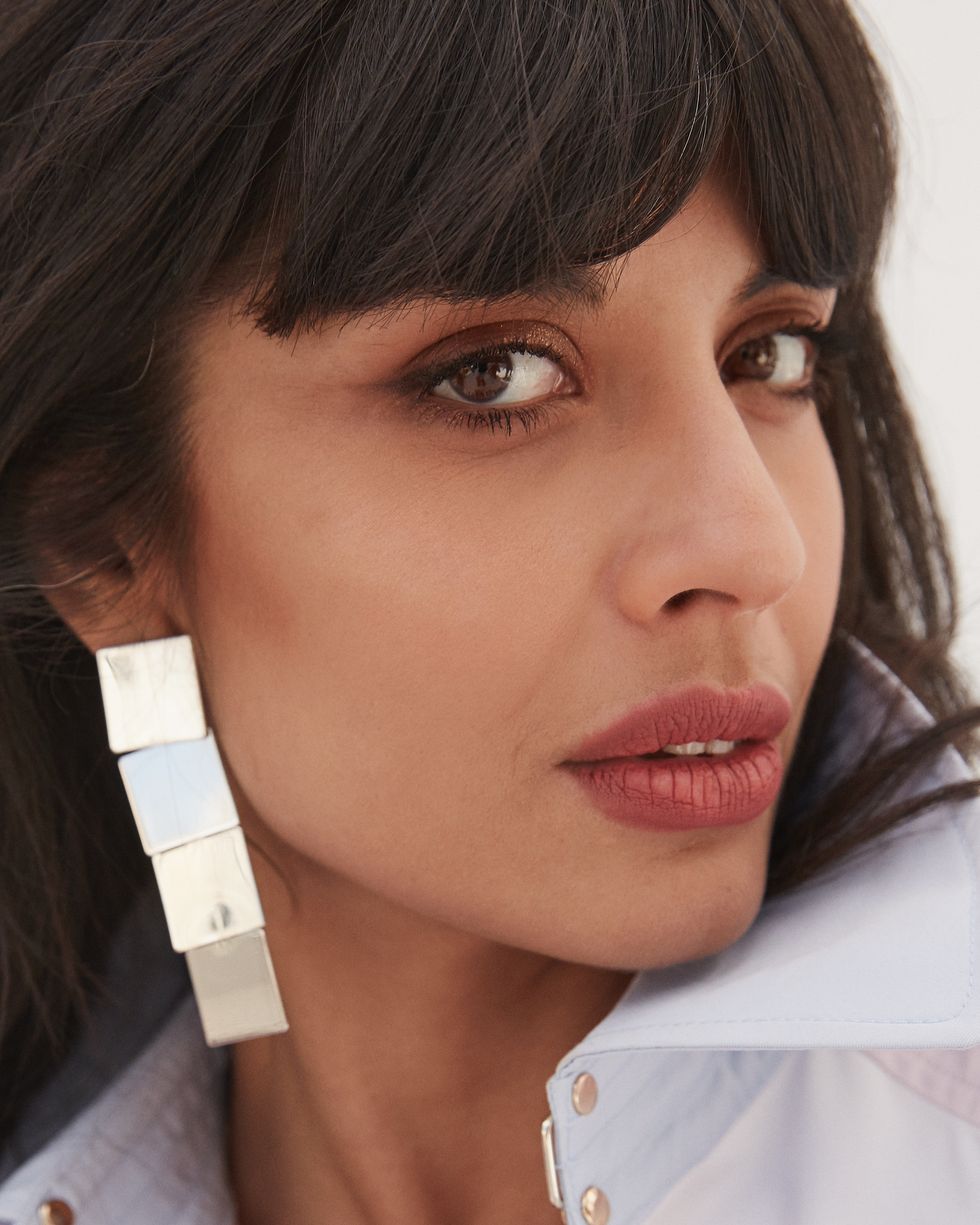 a close up of jameela jamil, wearing a pink trench coat by tommy hilfiger