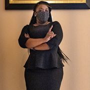 cori bush wears a mask and black dress and stands with her arms crossed after winning her congressional election