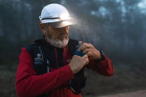 elderly man taking out from backpack soft flask silicone bottle to take a break after running and drink water