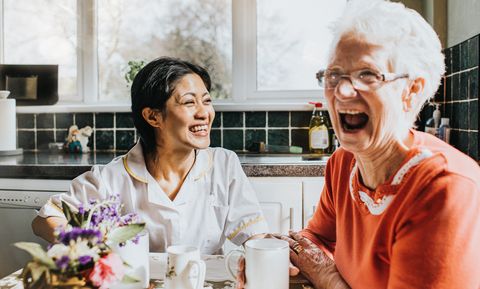 elderly woman cackles beside a giggling young care assistant