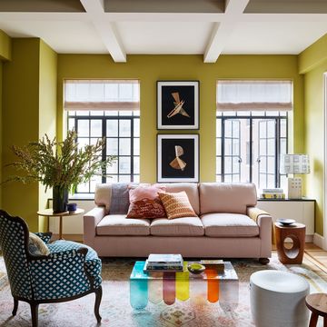 a living room with a pink sofa and a coloful glass coffee table and a blue and white armchair and tall french doors at the back and chartreuse painted walls